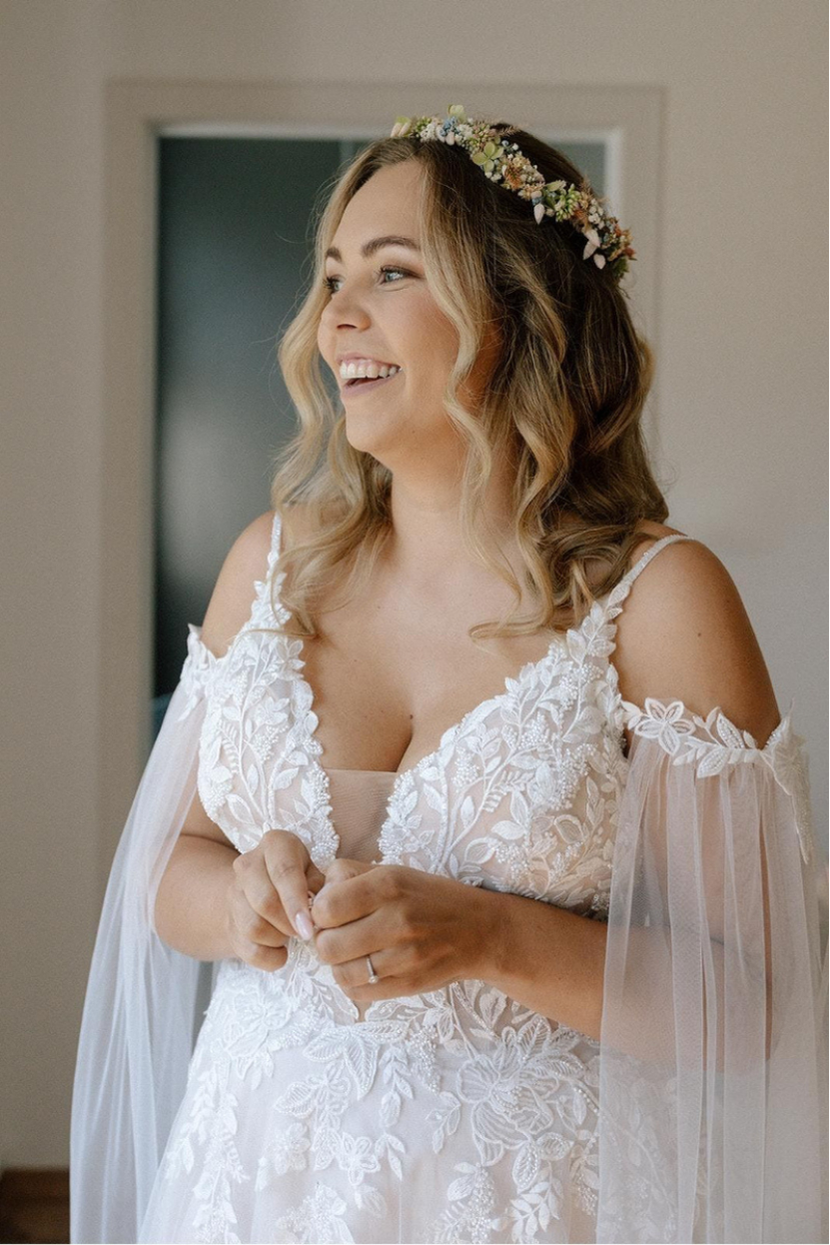 Lachende Braut in Brautkleid KIA-RA mit floraler Spitze Off-Shoulder-Ärmeln und Blumenkranz