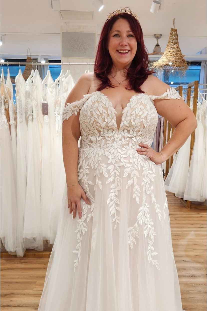 Lachende Curvy Braut im Hochzeitskleid SALO-ME mit Bardot-Ärmeln und floraler Spitze in Übergröße